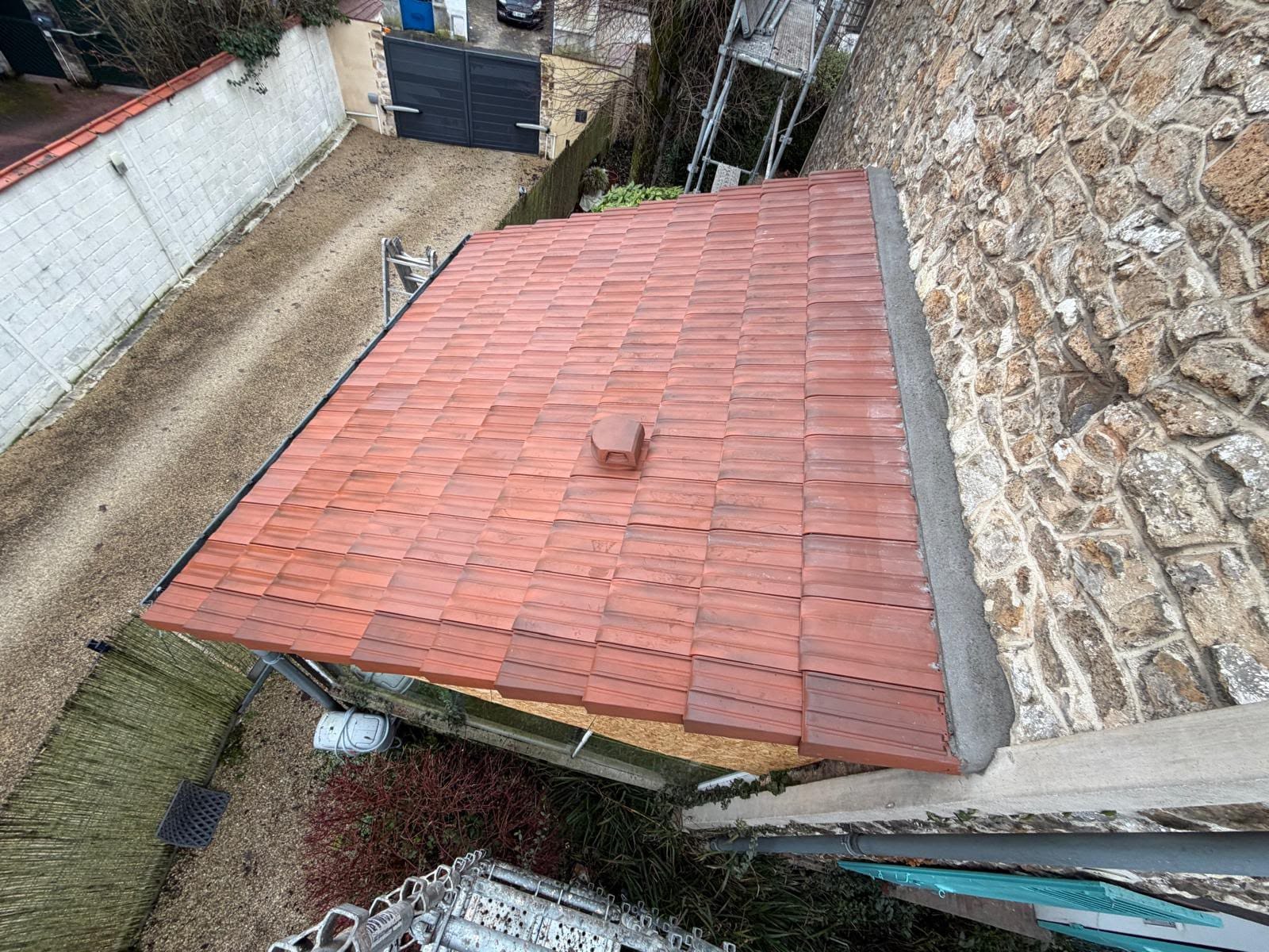 Couverture de garage neuve en tuiles mécaniques rouges le long d'un mur en meulière en Essonne