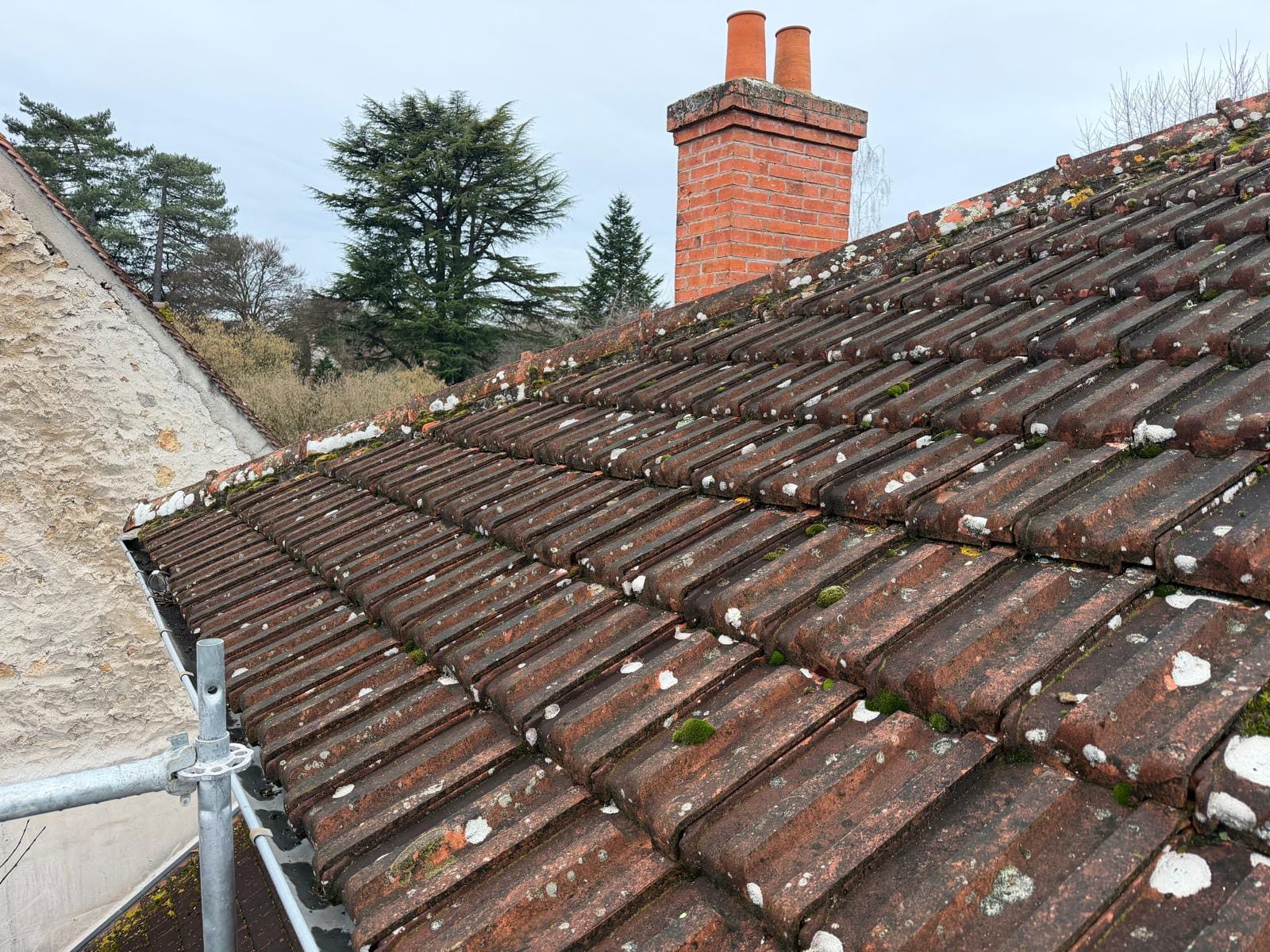 Tuiles anciennes moussues au pied d'une cheminée en brique avant rénovation de toiture en Essonne